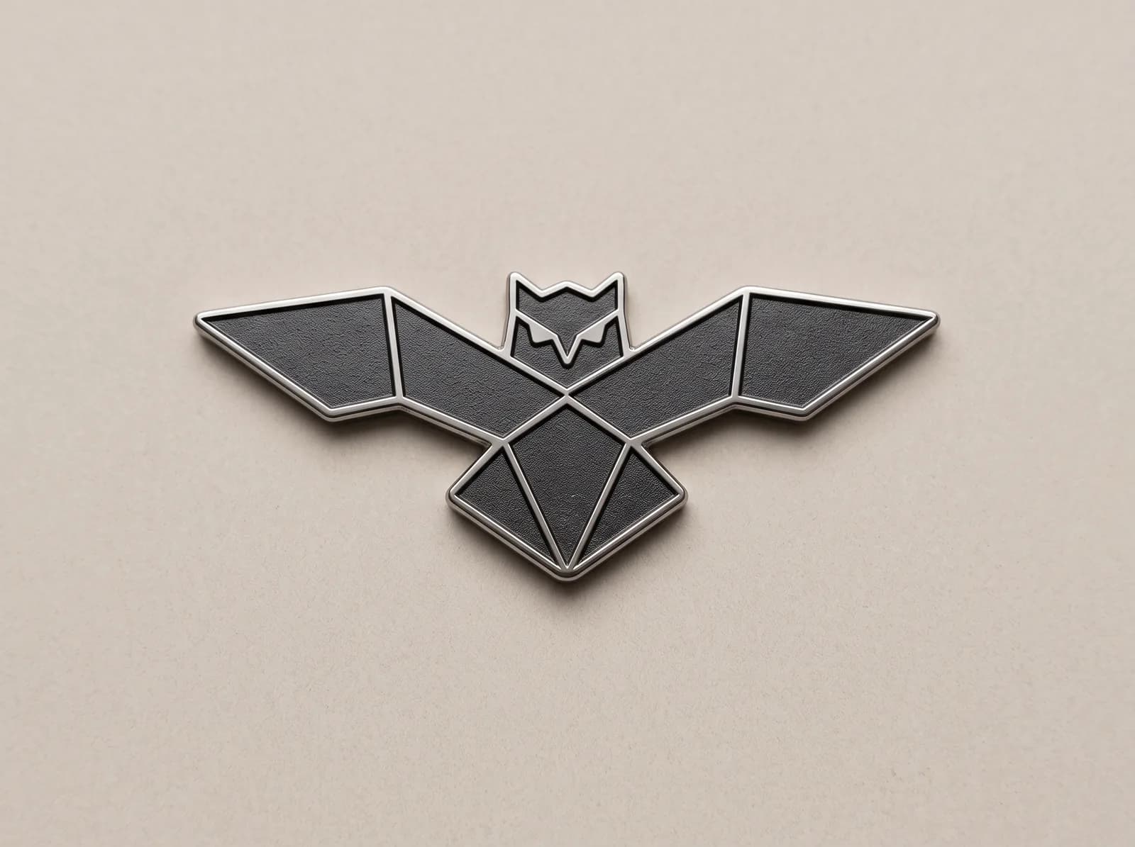 Wide silver badge cut to the shape of a geometric bat, with a dark fill