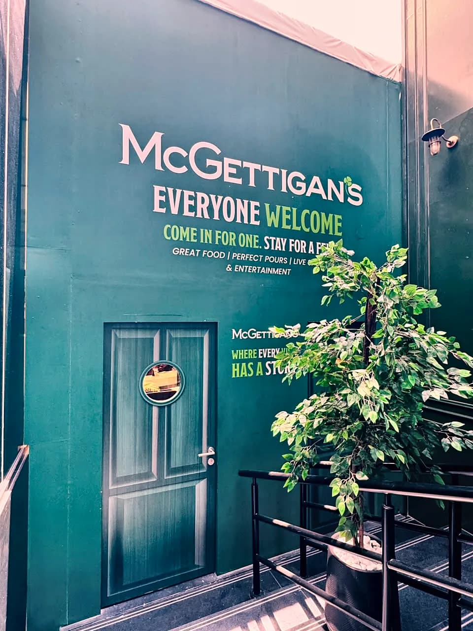 Dark green wall graphic with McGettigan's, Everyone welcome, Come in for one, stay for a while, around a door wrapped to look like a classic pub door