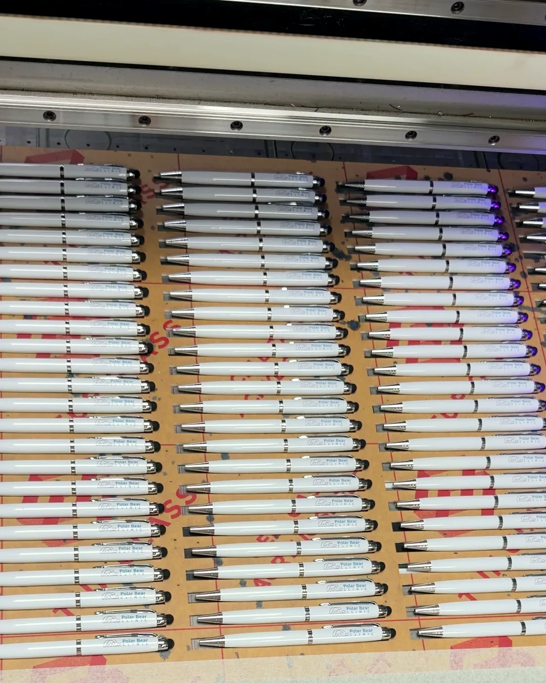 Rows of white pens in our UV printer, each printed with the Polar Bear Clinic logo