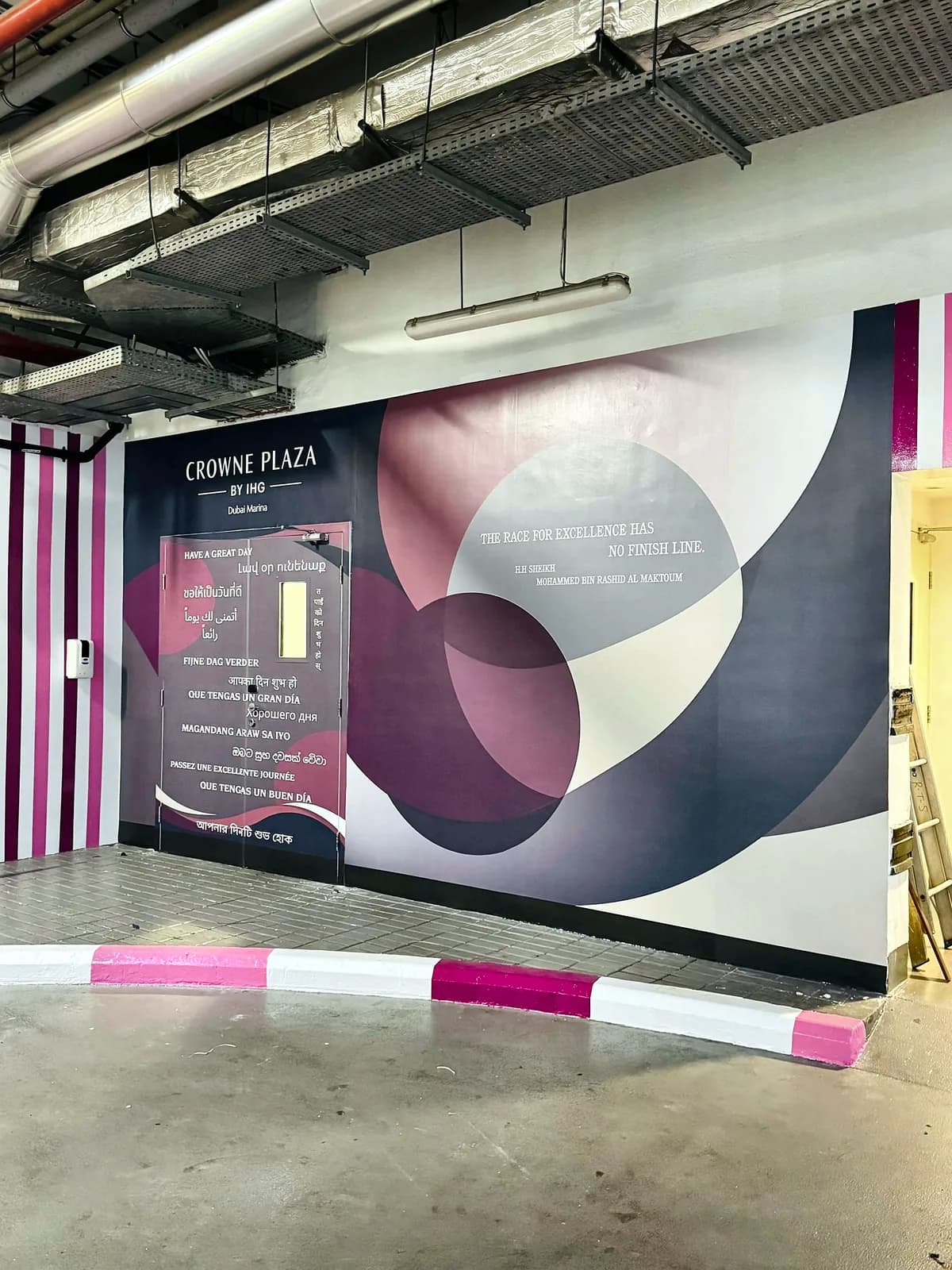 Car park wall at Crowne Plaza Dubai Marina covered in a large plum and grey graphic, with a wrapped door and greetings in many languages