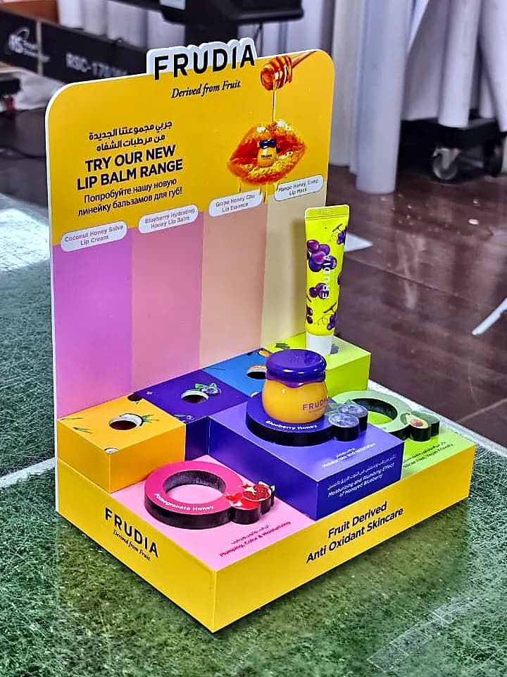 Yellow, pink and purple acrylic counter display for Frudia lip balms with printed product messages