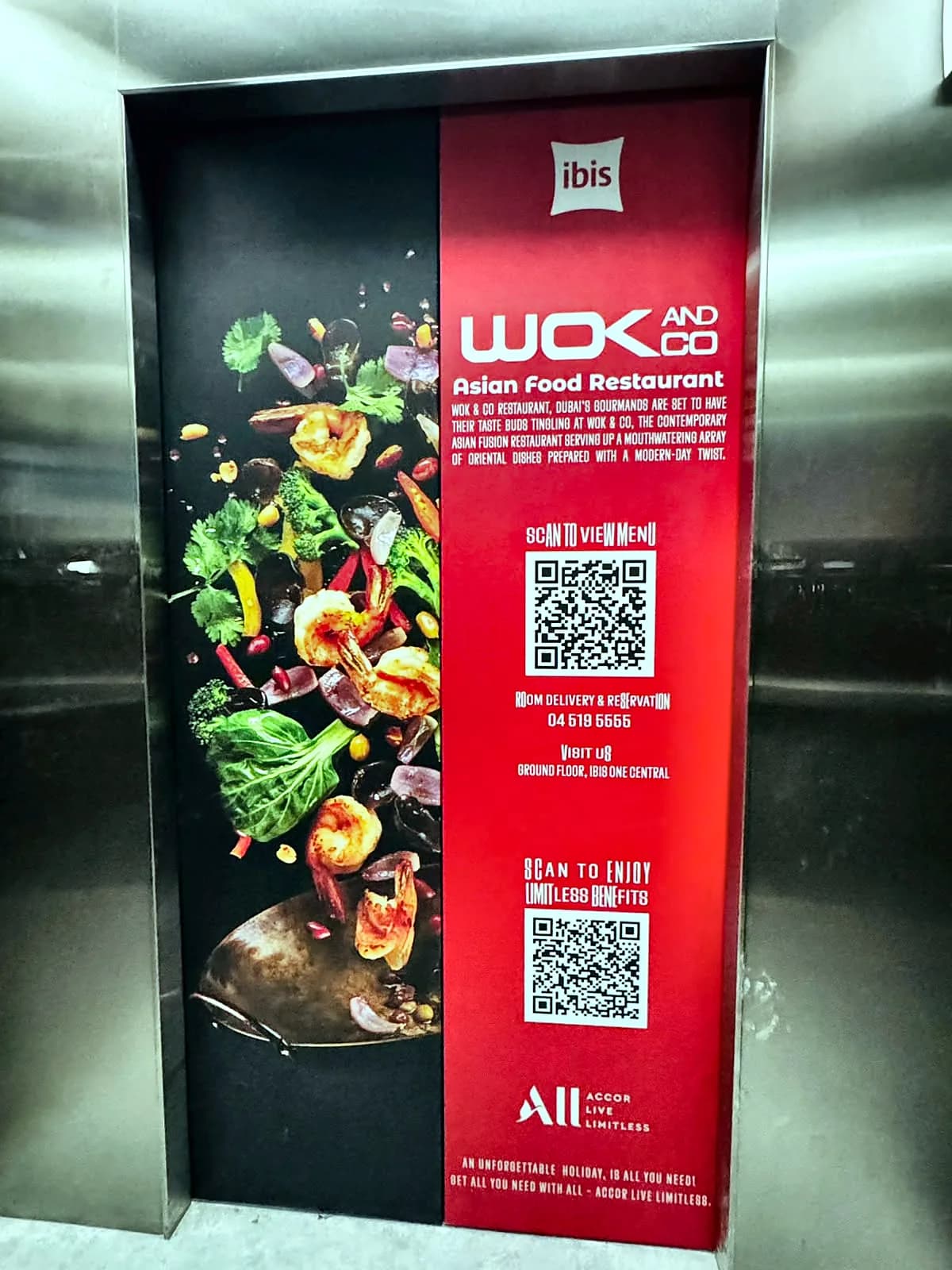 Lift doors at ibis One Central wrapped in a red and black Wok & Co Asian Food Restaurant graphic with fresh ingredients and two QR codes