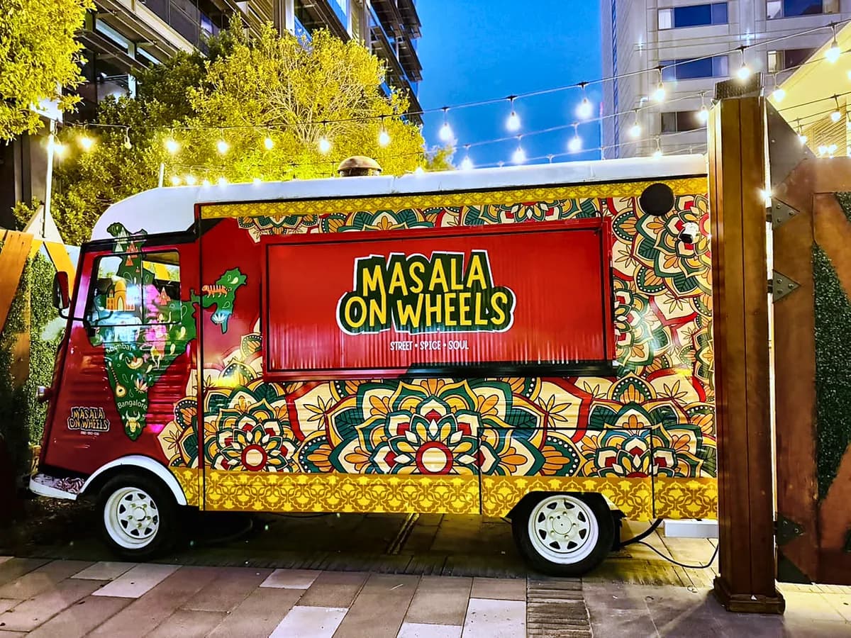 Red food truck fully wrapped in colourful patterned graphics with the Masala on Wheels name on the side
