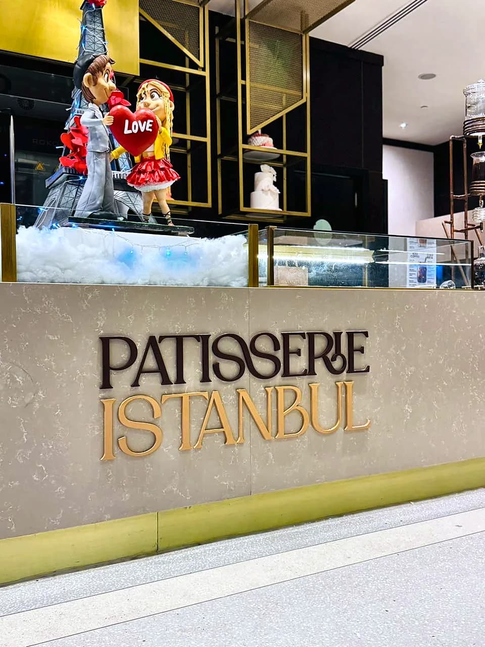 Raised Patisserie Istanbul lettering in dark and gold on a stone panel below a dessert display