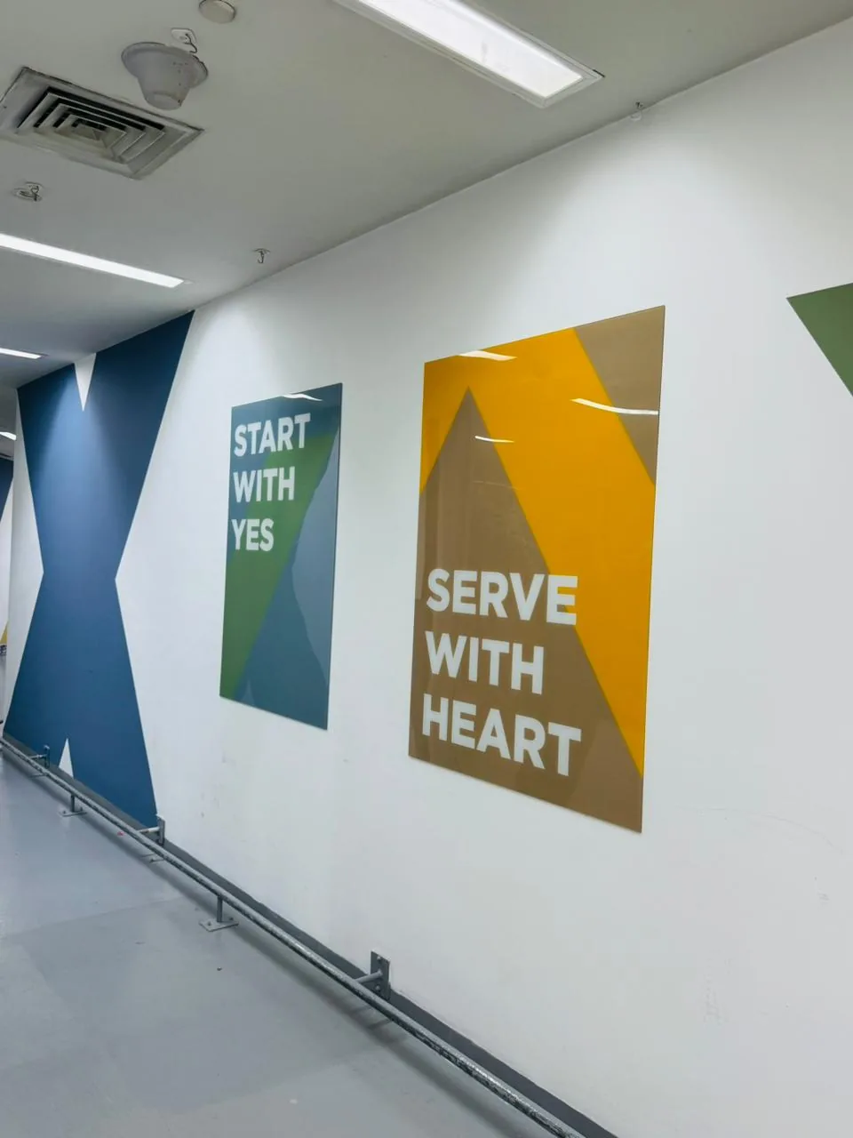 Two printed acrylic panels reading Start with yes and Serve with heart beside a large blue X wall graphic