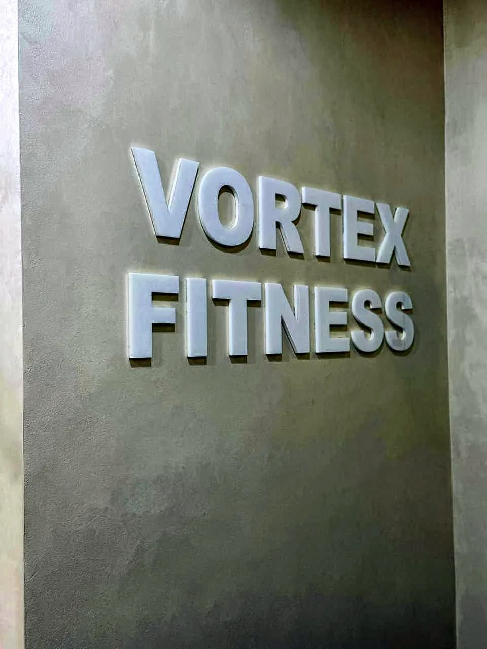 Raised silver 3D letters reading Vortex Fitness on a grey wall